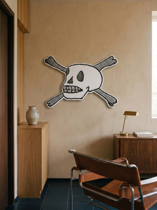 Forever shaped skull-and-crossbones canvas by Life Without installed on a plaster wall above a leather chair and wood credenza